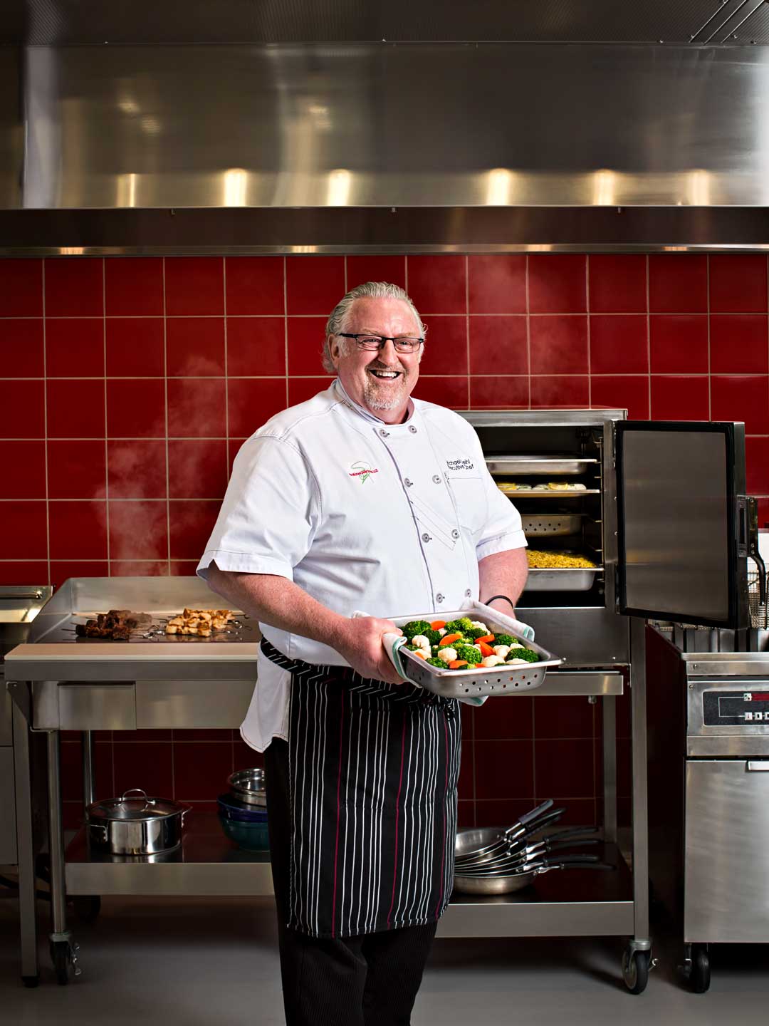 Chef stands in commercial kitchen with tray of food, Atlanta photography
