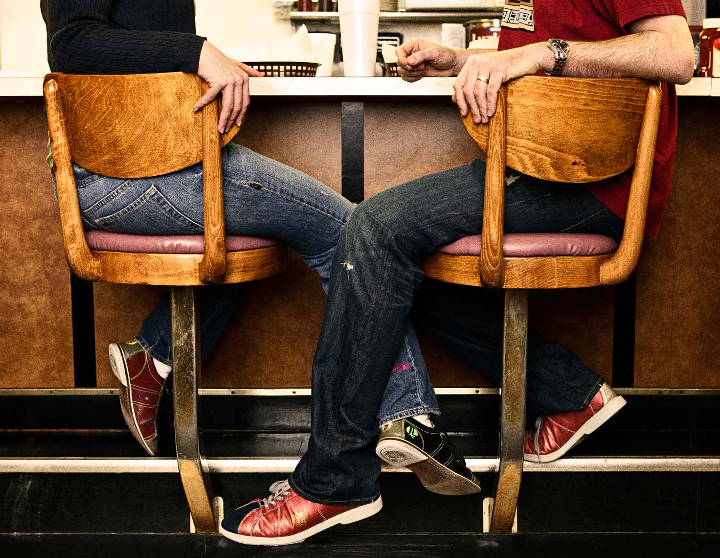 Couple sit on bar stools with legs intertwined. Photography Nick Burchell
