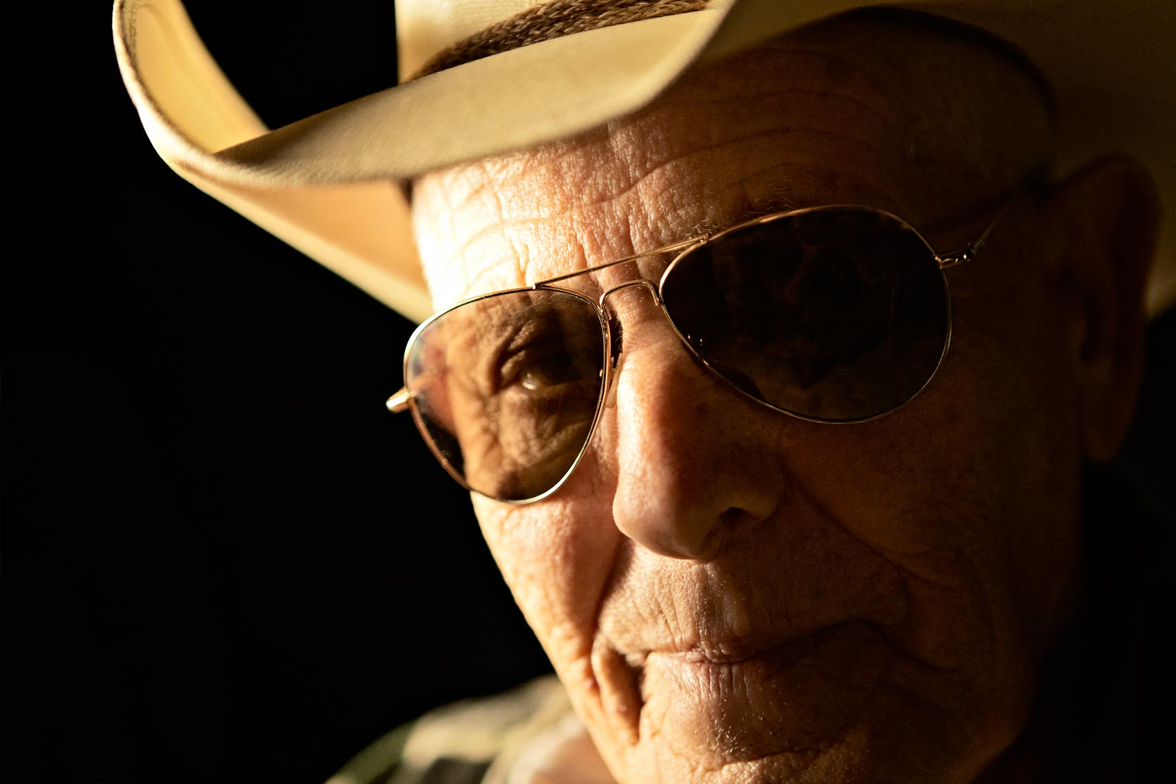 Tight portrait of old man wearing cowboy hat and sunglasses at night