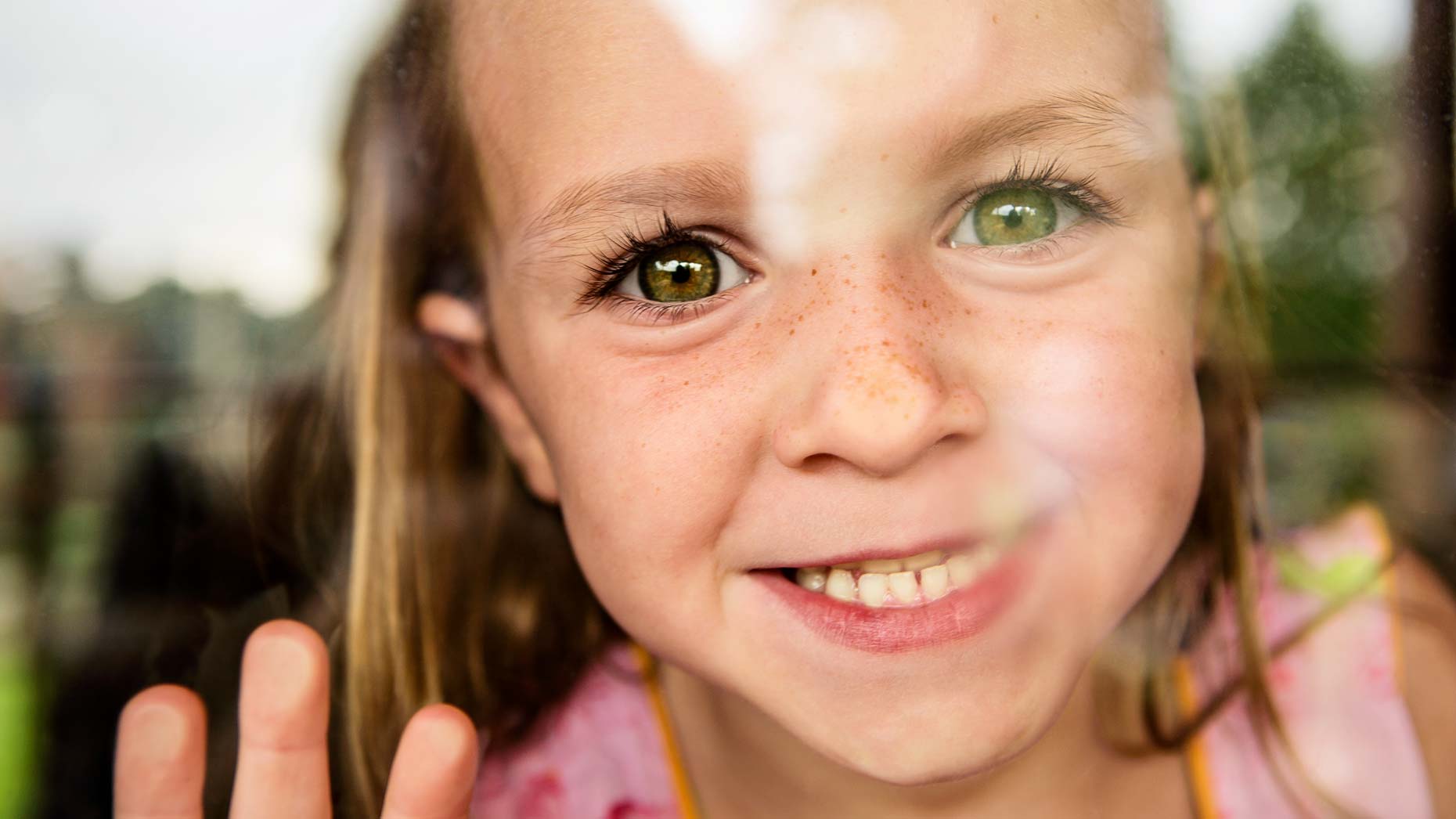 Young girl looks through window, smiling. Atlanta photography.